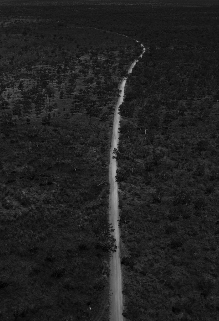Black and white drone view of long narrow road running through flooded terrain with dense woods