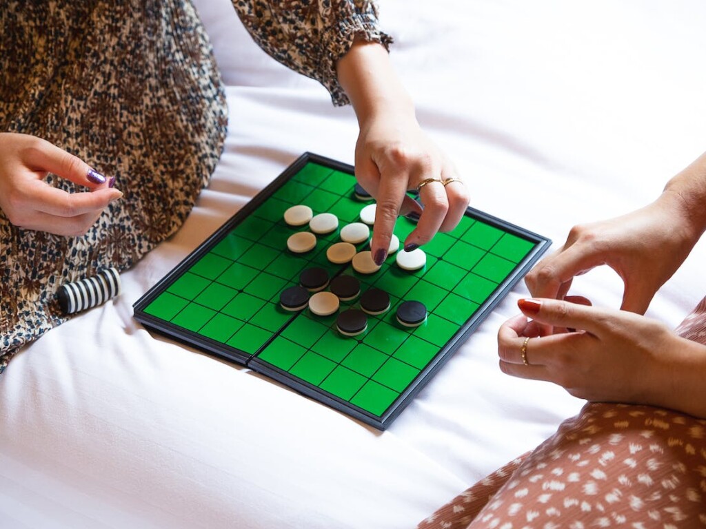 Crop unrecognizable women playing reversi game on bed