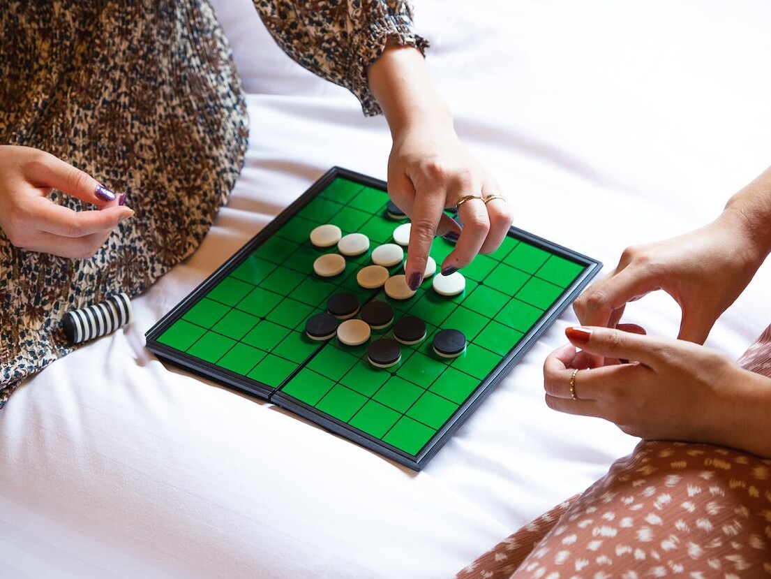 Crop unrecognizable women playing reversi game on bed